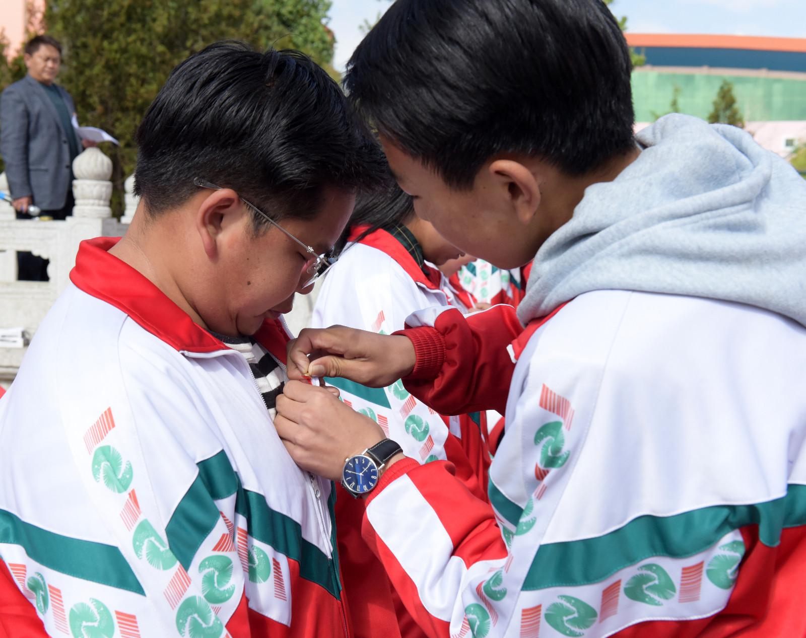 出席會議的領(lǐng)導(dǎo)和嘉賓為新團(tuán)員頒發(fā)團(tuán)員證，圖為老團(tuán)員為新團(tuán)員佩戴團(tuán)徽。