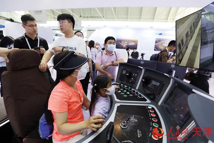 一位參觀者和孩子在天津軌道交通集團(tuán)展臺(tái)體驗(yàn)智能駕駛帶來(lái)的樂(lè)趣。人民網(wǎng)記者 孫翼飛攝
